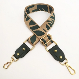 Detail of adjustable canvas bag strap with dark green geometric patterns and gold metal clips