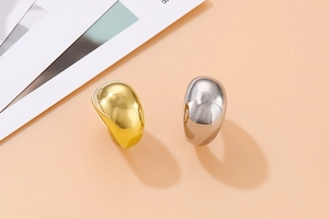 Close-up of gold and silver teardrop rings with high-polish finish on orange background