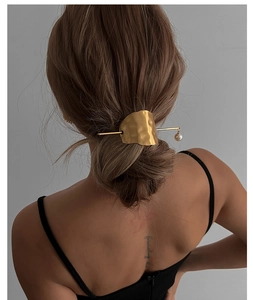 Detail of irregular gold hair pin with pearl pendant on elegant bun hairstyle