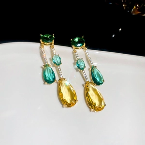 Détail de boucles d'oreilles à pompons avec zircons vert et jaune sur plaqué or