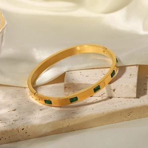 Detalle de brazalete dorado con piedras verdes rectangulares sobre una base de piedra