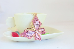 Detailed view of a golden butterfly keychain with pink crystals on a tea cup handle