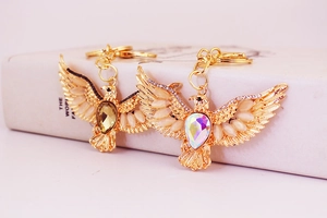 Macro shot of two gold eagle keychains with rhinestones and large gemstones on a white book