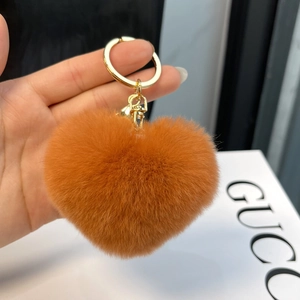 Close-up of orange-brown heart-shaped rex rabbit fur keychain held in hand with gold ring