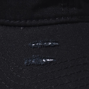 Macro view of distressed brim details with fringe and white fibers on a black cotton cap
