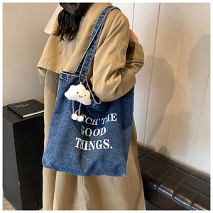 Détail du sac cabas en jean bleu avec texte blanc et pendentif nuage en peluche