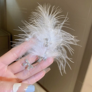 Detail of white feather ear cuff with rhinestone bowknots and elegant pearl accents
