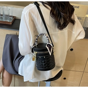 Detail of black woven bucket bag with gold padlock and silk scarf on a model