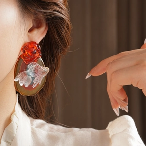 Detailed close-up of a large artistic earring with red rose and clear goldfish pendant