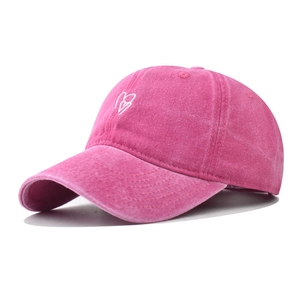 Detail of pink washed cotton baseball cap featuring embroidered double heart design