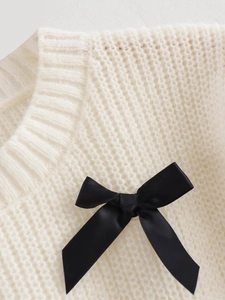 Detail eines weißen Strickpullovers mit einer kontrastierenden schwarzen Schleife am Ausschnitt