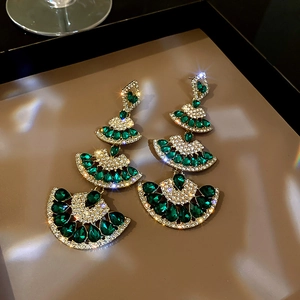 Detailed view of luxury fan-shaped earrings with green gems and glittering crystals