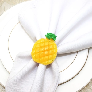 Detail showing a yellow pineapple napkin ring on a white napkin over a gold-rimmed plate