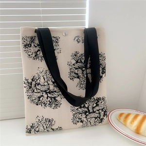 Detail of floral knit tote bag featuring a magnetic snap closure and black wide handles