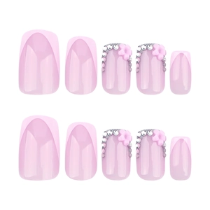 Pink French press-on nails set with 3D floral accents and rhinestones on white backdrop