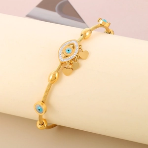 Macro view of gold cable bracelet featuring evil eye charm and hanging gold hearts