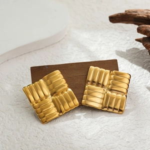 Macro detail of square gold stainless steel earrings with woven texture on wood