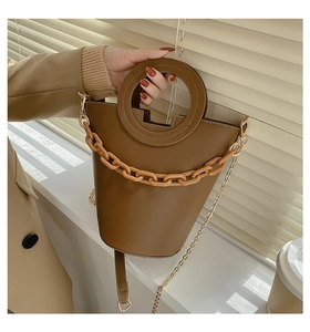 Detail of brown bucket bag featuring a unique circular cutout handle and chunky plastic chain