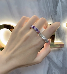 Detail view of emerald cut purple and white gemstone ring on model's finger with marble background
