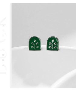 Macro shot of silver minimalist stud earring with green enamel leaf design on white ceramic