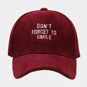 Close-up of wine red corduroy baseball cap with white Don't Forget To Smile embroidery