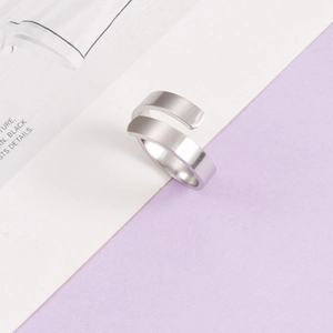 Minimalist silver crossover open ring in brushed stainless steel on a magazine background
