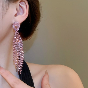 Close-up of elegant pink rhinestone tassel earrings worn by a model in warm lighting