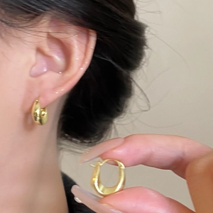 Detail view of gold-plated U-shaped chunky hoop earrings worn to show style and size