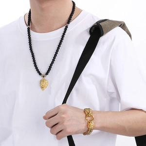 Detailed view of men's black onyx bead necklace and gold lion head bracelet on model