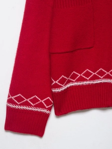 Détail du cardigan en maille rouge avec motifs en losange blancs et coutures brodées