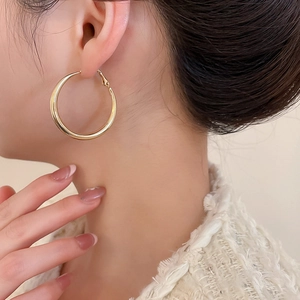Close-up of model wearing large high-polished gold hoop earrings with minimalist design