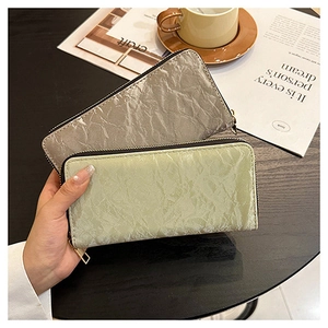 Detail of wrinkled metallic silver and green long zip wallets held in a cafe setting