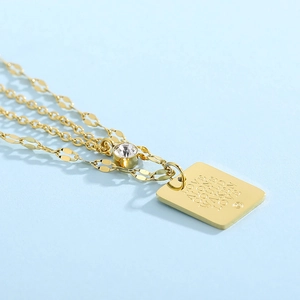 Detail of gold multilayer necklace featuring engraved pendant and crystal charm inlay