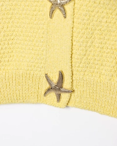 Gros plan sur une robe en maille jaune avec bouton décoratif en forme d'étoile de mer