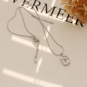 Détail d'un collier chaîne serpent argentée avec pendentif tulipe sur fond neutre