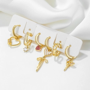Golden earrings set featuring bowknots, pearls, and hearts on a white silk background