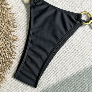 Gros plan du bas de bikini noir avec anneaux dorés sur fond de tricot crème