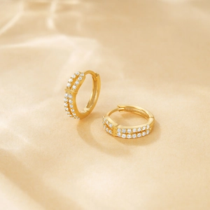 Detail shot of golden double-row pavé twisted hoop earrings on beige fabric background