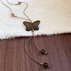 Détail d'un pendentif papillon en bois sur cordon marron avec des perles foncées