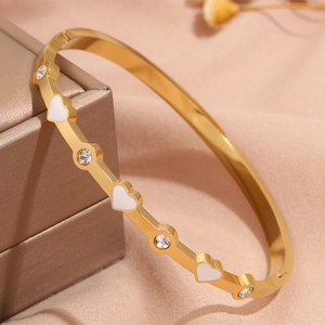 Vista macro di un bracciale dorato con cuori in smalto bianco e zirconi scintillanti