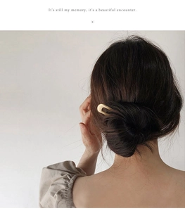 Detail of a minimalist gold U-shaped metal hair pin securing a bun on a woman's head
