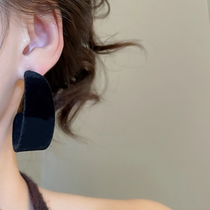 Gros plan d'une boucle d'oreille créole noire floquée en forme de C portée par un modèle