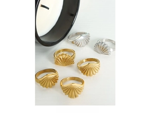 Macro detail of scallop shell rings in gold and silver finish on a white wood surface