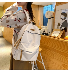 Detail of minimalist cream backpack with brown leather accents and front zipper pocket