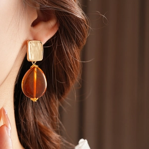 Close-up of vintage gold square stud with amber resin teardrop earring worn by a model