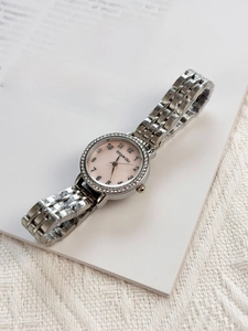 Detail of silver metal strap watch with pink dial and diamond bezel on a vintage book