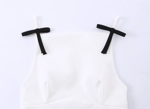 Detail van een witte camisole top met subtiele zwarte strikjes op de bandjes