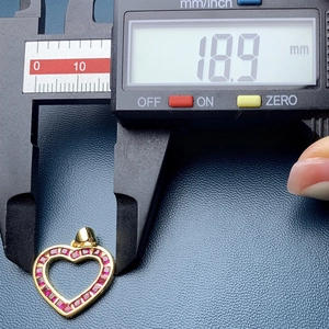 Macro view of a 18.9mm heart-shaped gold pendant with red gemstone using a caliper measurement