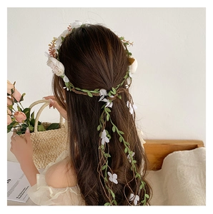 Detail of white flower crown with green leaves and vine tassels on model hair