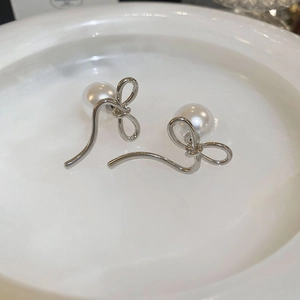 Macro detail of elegant silver bow earrings with round white pearls on a white ceramic tray